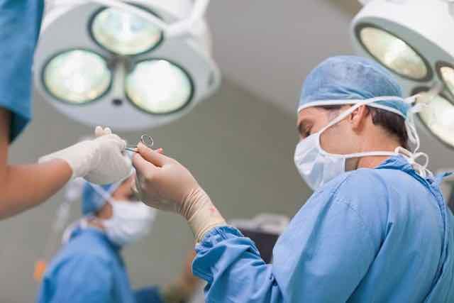 médico recebendo uma tesoura cirurgica de enfermeira