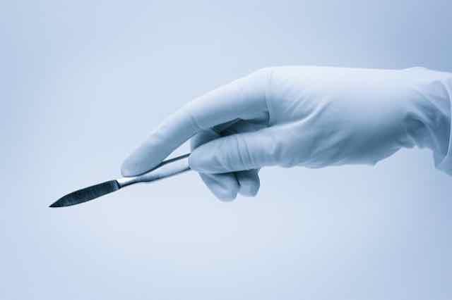 luva cirurgica segurando um bisturi