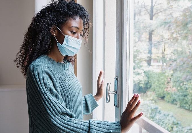 mulher de máscara na janela e os impactos da pandemia na saúde dos brasileiros