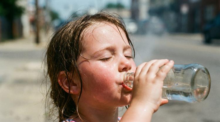 Menina ingerindo água debaixo de sol quente